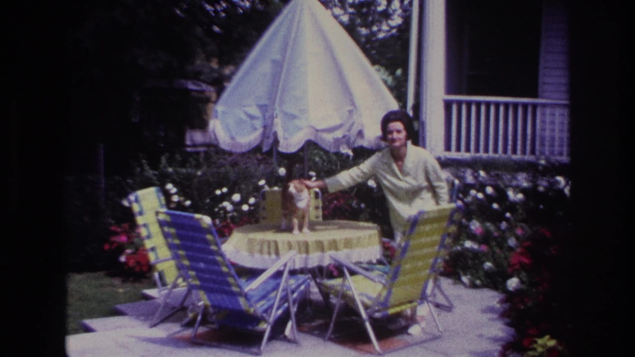 Woman smiles toward the camera while holding a cat on a patio table.