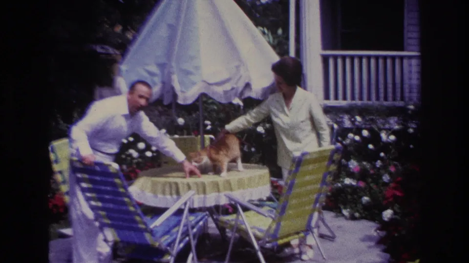 Rockaway Beach 1967 patio frame showing a woman handling a ginger cat on a table while a man sits nearby.