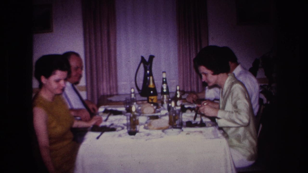 1967 Rockaway Beach home-movie frame showing four adults at a dining table in a private interior with bottles, glasses, and a white tablecloth.