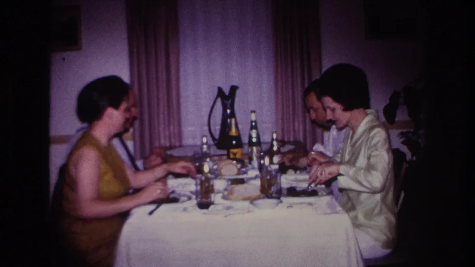 1967 Rockaway Beach family dinner frame showing adults seated in profile around a set table inside a private home.