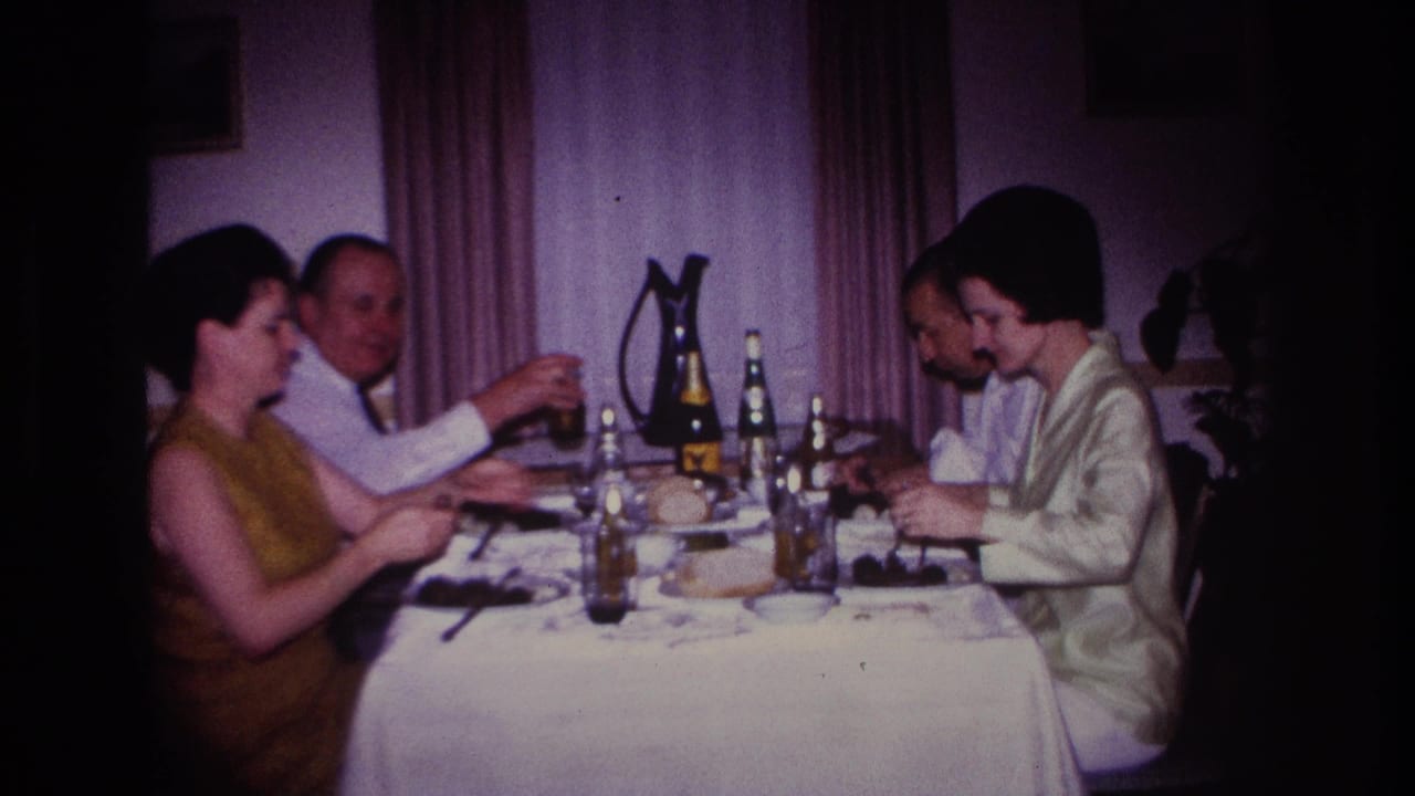 Adults at the table raise or hold glasses while seated beside bottles and plates.
