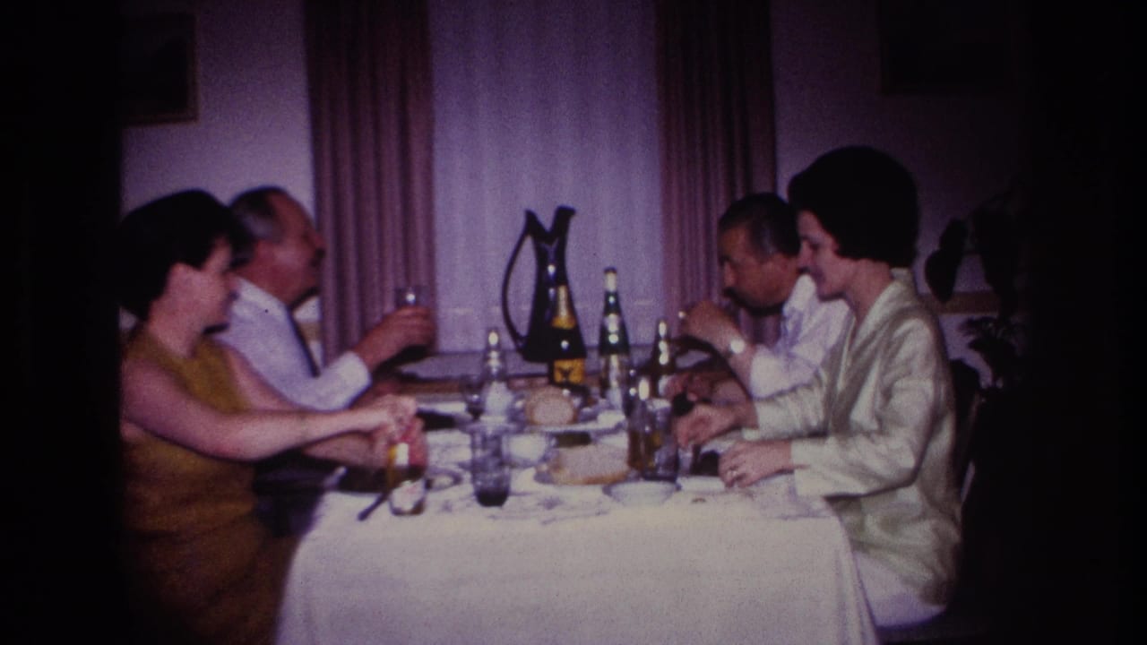 1967 Rockaway Beach home-movie frame showing four adults at an indoor dining table with drinks and tableware.