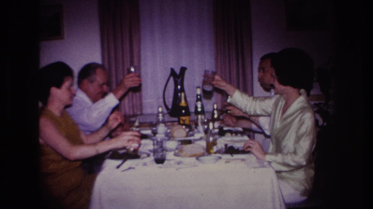 Four adults seated at a dinner table raise glasses in a dim private interior.