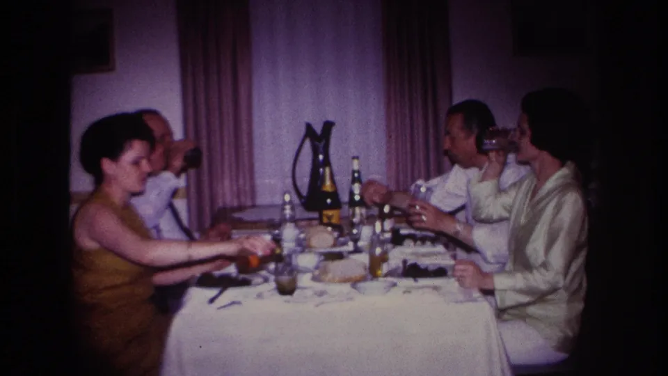 1967 Rockaway Beach home-movie frame showing adults drinking and conversing at a private dinner table.