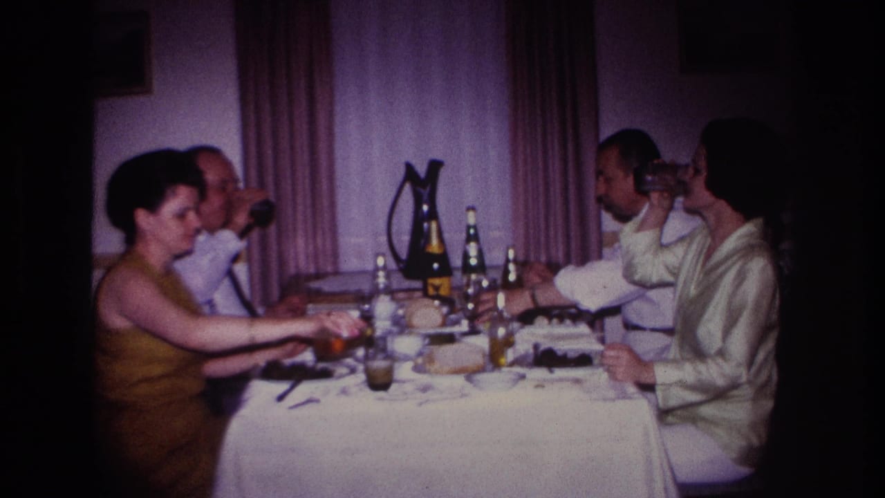 1967 Rockaway Beach home-movie frame showing four adults at a white-clothed dinner table with drinks and tableware.