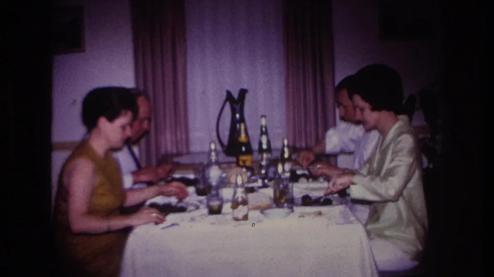 1967 Rockaway Beach frame of two couples finishing or continuing dinner at a softly lit table with bottles and glassware.