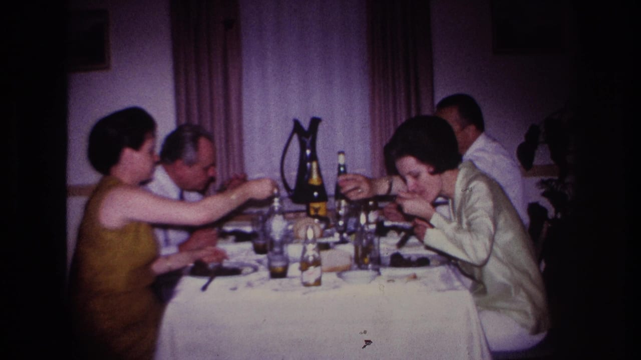 1967 Rockaway Beach home-movie frame showing adults eating and drinking around a white-clothed dining table.