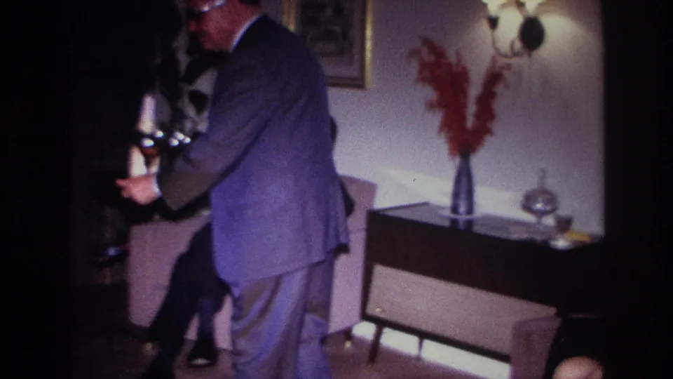 1967 Rockaway Beach home interior with a suited man near seated guests, cocktail glasses, a sofa, and mid-century decor.