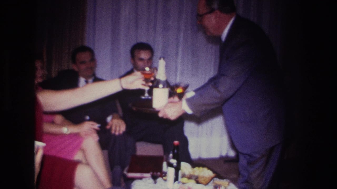 1967 Rockaway Beach home-movie frame with suited adults and a woman in red as a man offers cocktails from a tray.