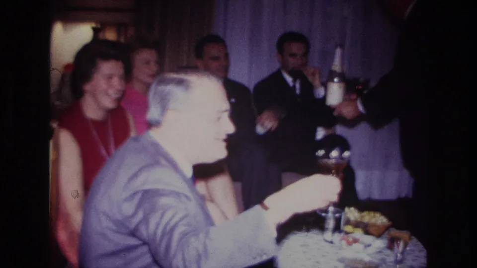 A 1967 Rockaway Beach party frame shows adults laughing at a table as a server presents drinks and bottles in a private room.
