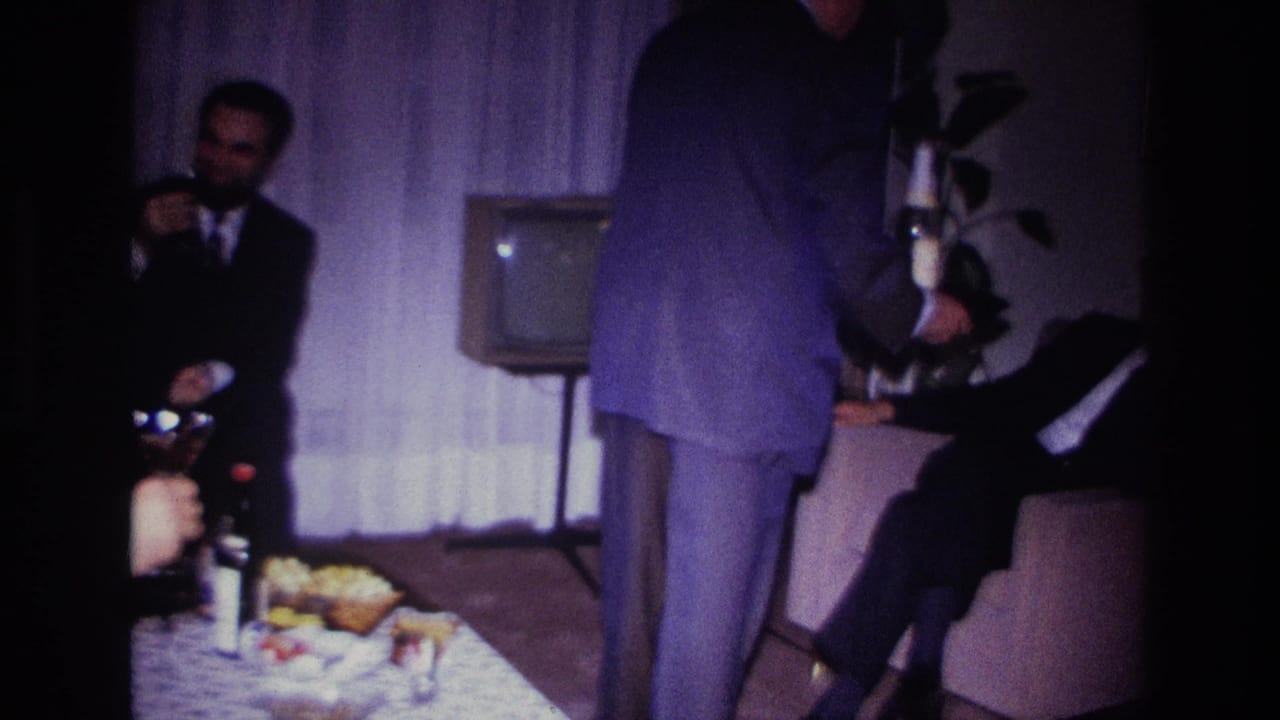 Suited men in a 1967 Rockaway Beach living room hold glasses as a standing figure crosses the handheld frame.