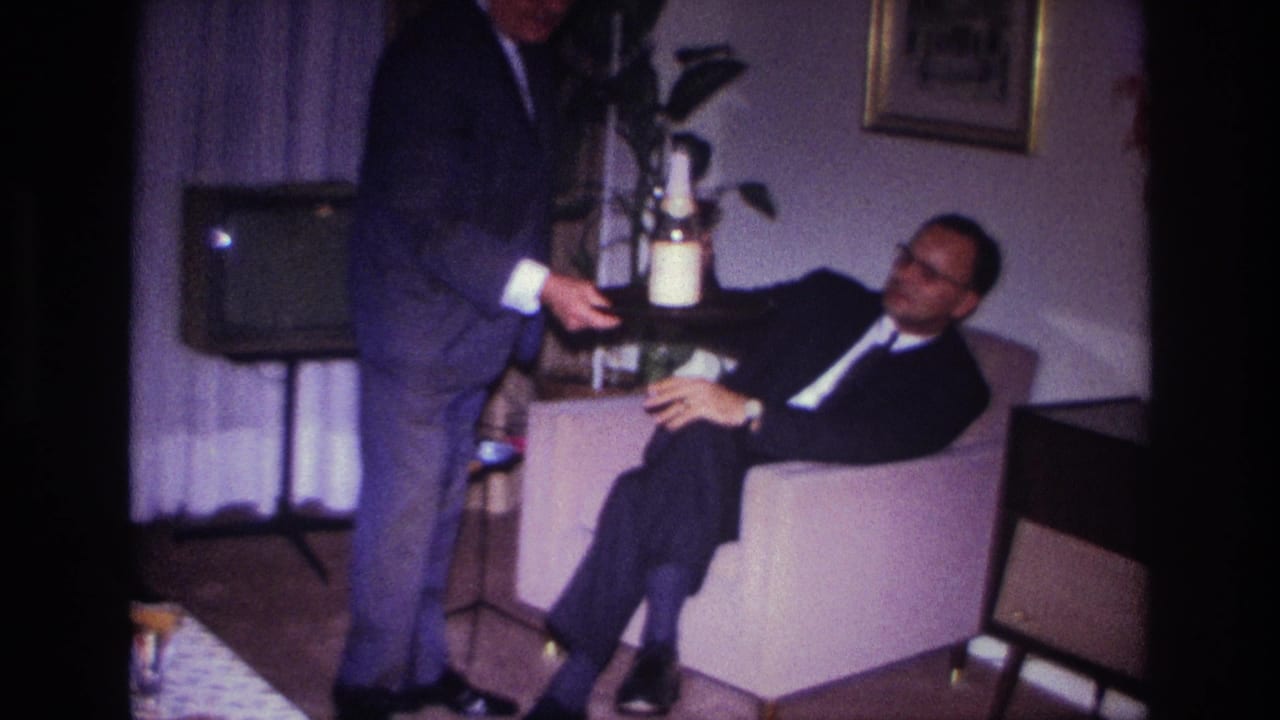1967 Rockaway Beach home-movie frame showing a suited man serving drinks to a seated man in a private living room.