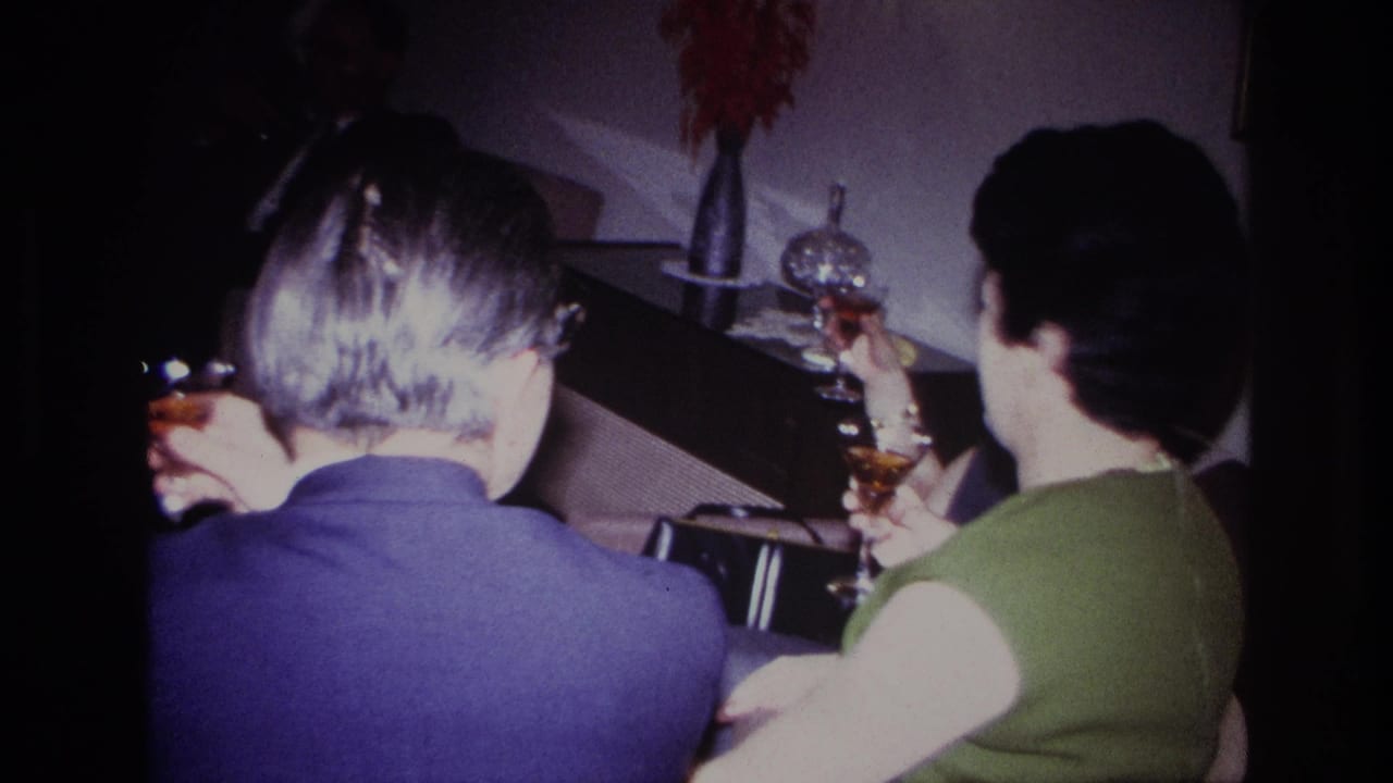 1967 Rockaway Beach home-movie frame of adults raising cocktail glasses in a dim private living room.