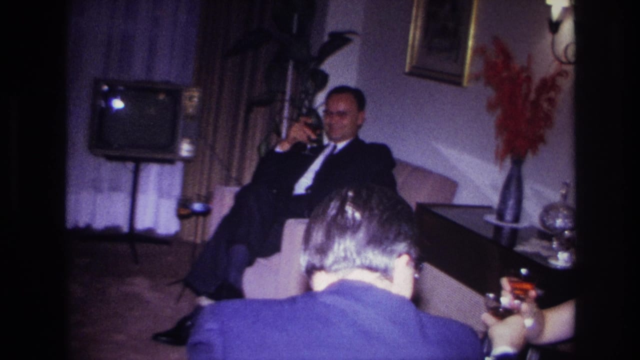 1967 Rockaway Beach home-movie frame showing dressed adults seated with drinks in a private living room near a small television.