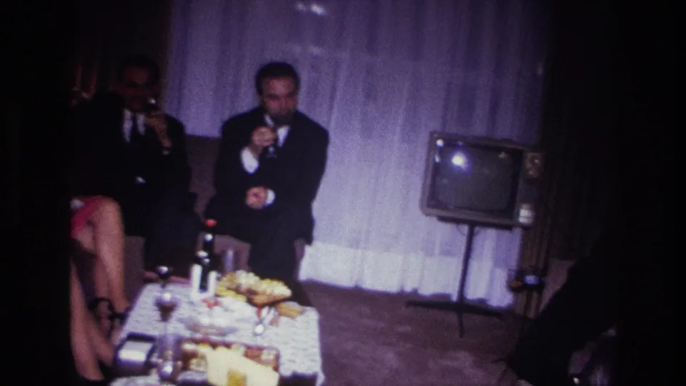 Adults in formal evening clothes gather around a food table in a 1967 Rockaway Beach private interior.