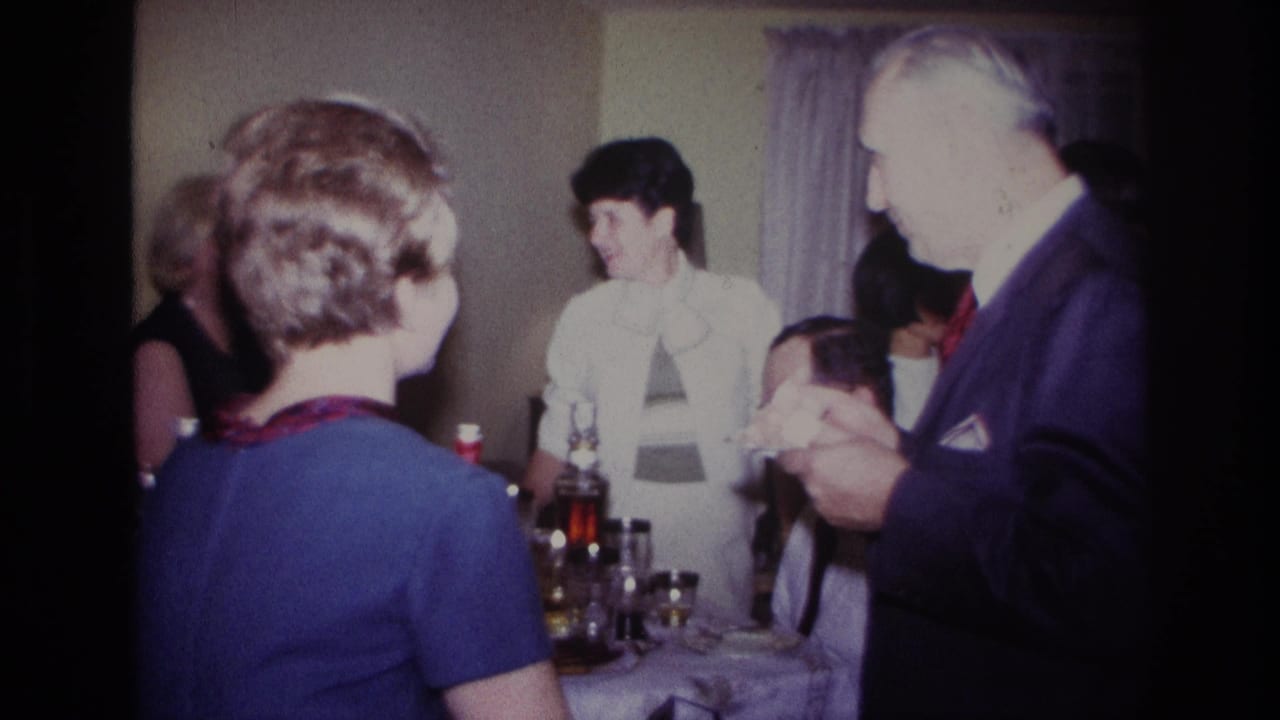 1967 Rockaway Beach home-movie frame showing adults around a dining table with drinks in a private interior.