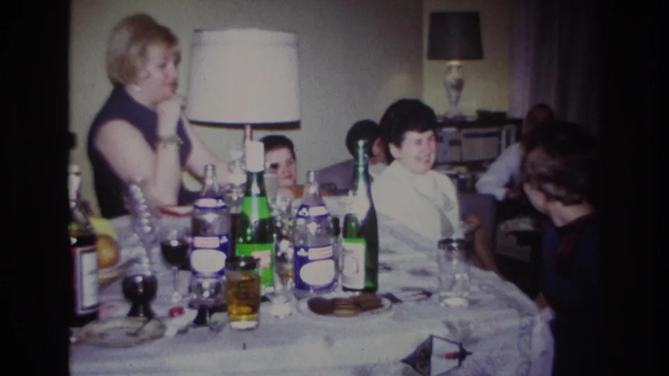 1967 Rockaway Beach family interior showing adults and a child beside a dining table with drinks and a lamp.