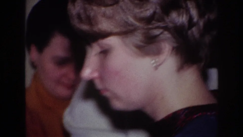 1967 Rockaway Beach home-movie frame showing a woman at a piano in a living room as two seated women watch behind her.
