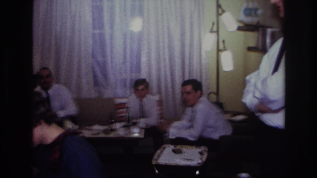 Guests sit around small tables in a living room while others stand nearby.