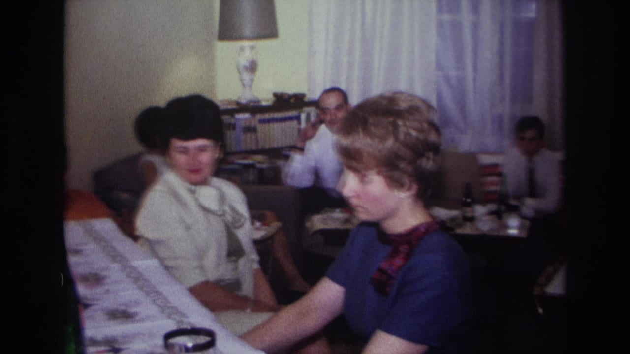 1967 Rockaway Beach home-movie frame showing a woman at a piano with family members seated around a living room.