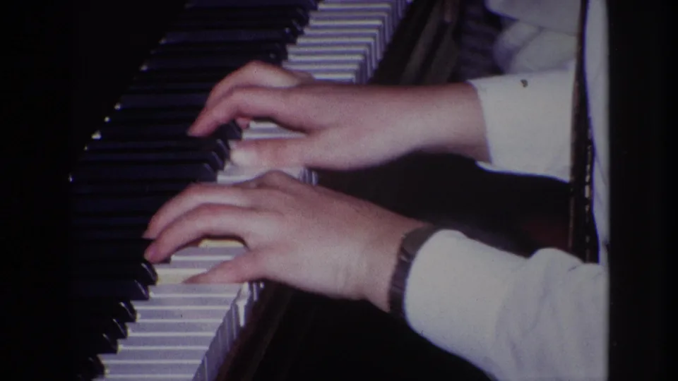 Close-up of hands over a piano keyboard in the documented 1967 Rockaway Beach home-movie setting, with the player mostly out of frame.