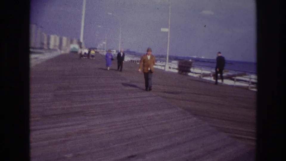 Rockaway Beach, New York boardwalk in 1967 with a smoking pedestrian in a brown jacket and several adults in the background.