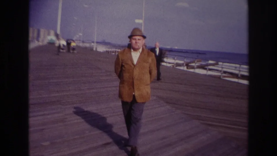 A closer 1967 Rockaway Beach view shows the man walking along the boardwalk with his shadow across the planks and the sea beyond the rail.
