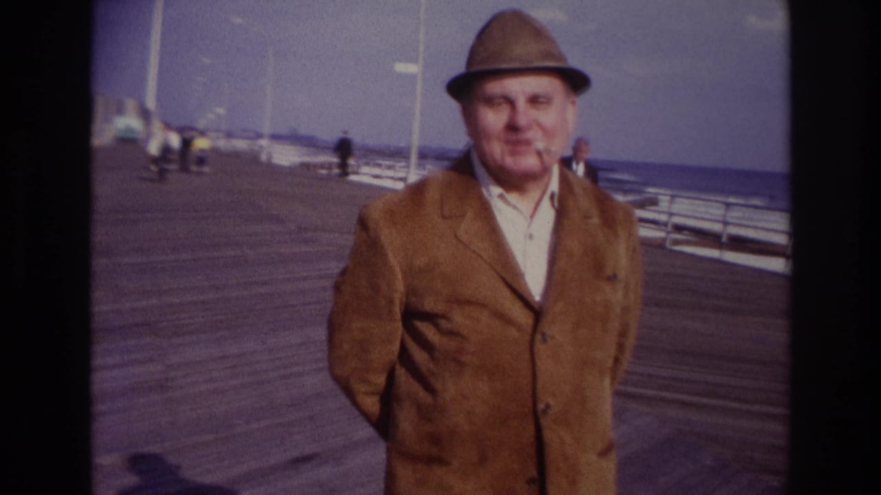 Closer view of a man in a brown jacket and hat on the boardwalk by the water.