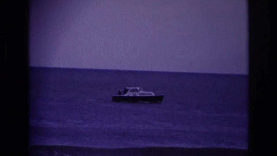 A small boat sits offshore at Rockaway Beach in 1967, framed in soft, saturated 8mm color with the ocean horizon behind it.