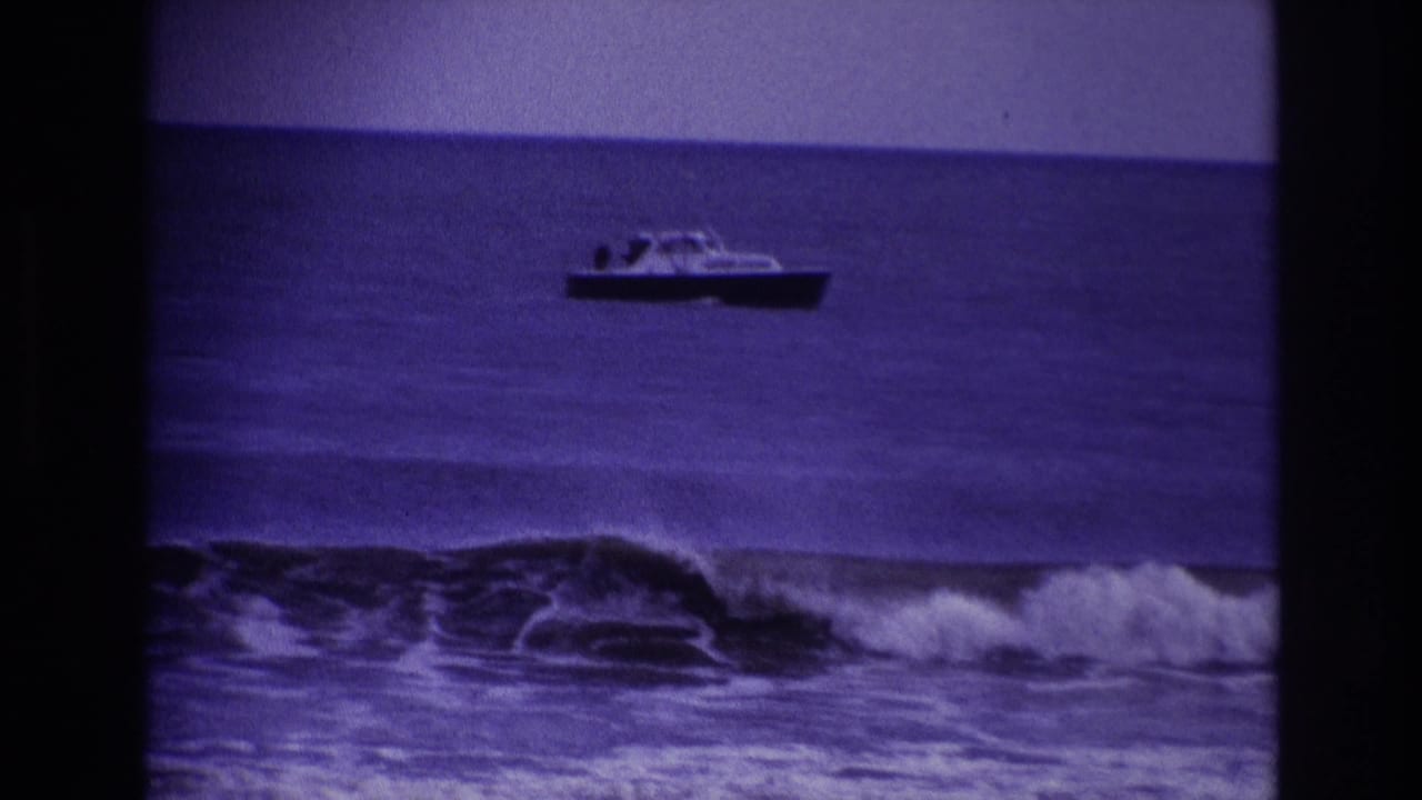 Small motorboat offshore beyond breaking waves, framed by dark film borders.