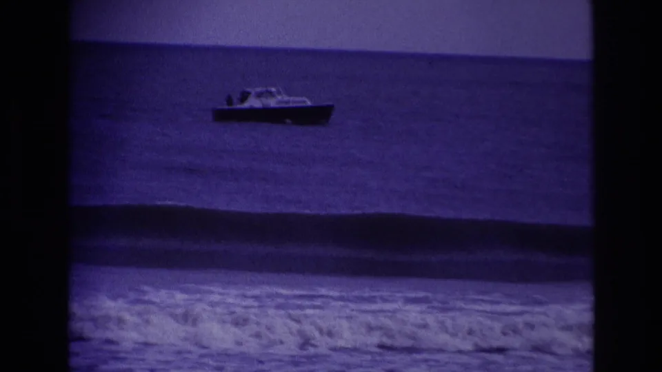 1967 Rockaway Beach 8mm frame showing a motorboat offshore, a dark rolling swell, and white surf under a purple film cast.