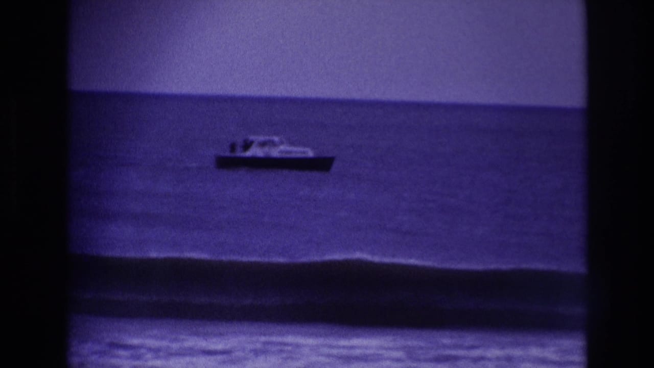 1967 Rockaway Beach home-movie frame showing a small motorboat offshore under a blue sky and above incoming surf.