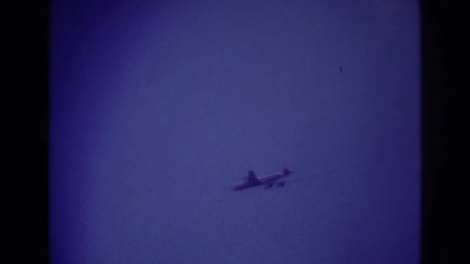1967 Rockaway Beach frame showing a small airplane crossing the blue sky, with no ground detail visible.