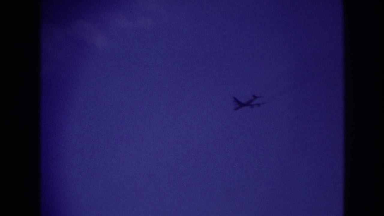 A small airplane silhouette crosses the deep blue sky in the supplied Rockaway Beach 1967 home-movie clip.