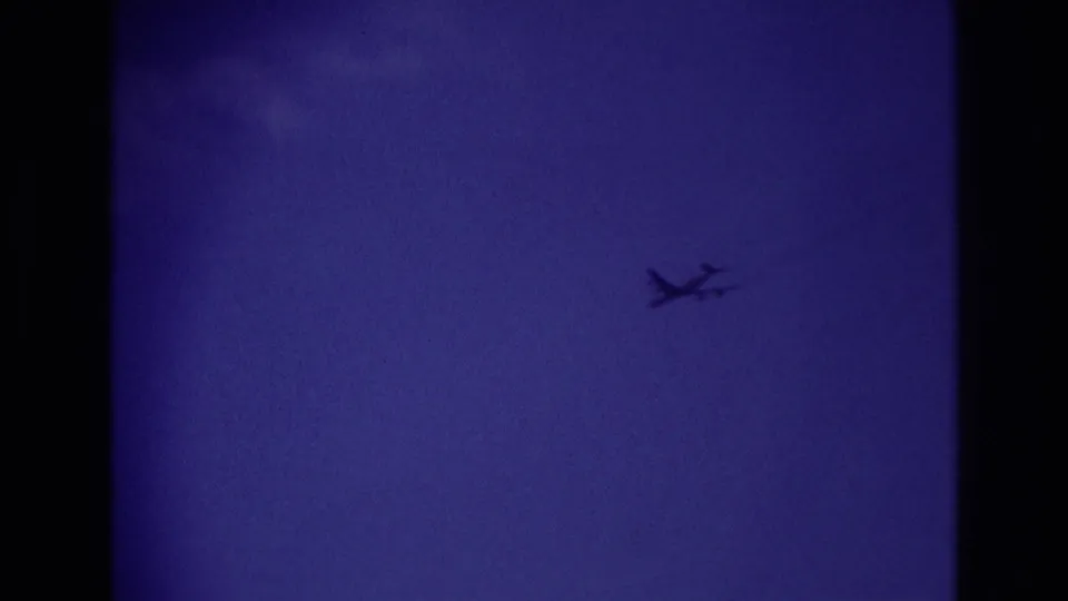 A small airplane silhouette crosses the deep blue sky in the supplied Rockaway Beach 1967 home-movie clip.