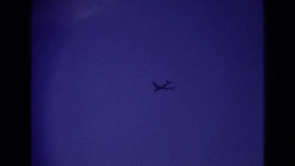 The airplane remains visible as a small dark shape against the purple-blue sky, framed by heavy 8mm film borders.