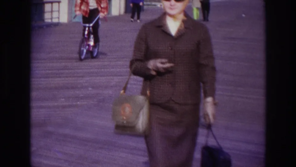 The final frame crops the woman close to camera on the 1967 Rockaway Beach boardwalk, with a bicyclist and other pedestrians in the background.