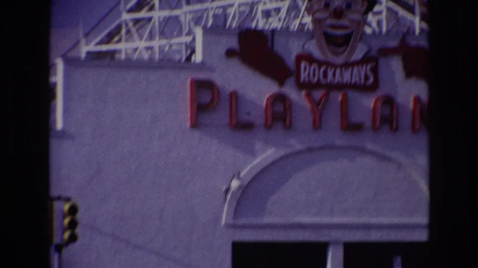 Close 8mm frame of the Rockaways Playland facade, showing the clown sign, red Playland letters, and part of the arched doorway.