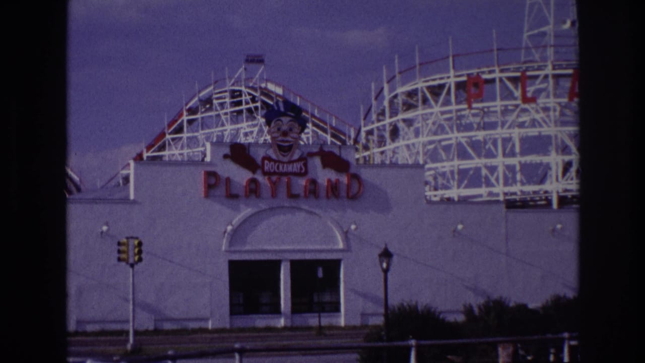 1967 Rockaway Beach Playland entrance seen from across the street, with red signage, a clown mascot, and white roller-coaster structure rising above the facade.