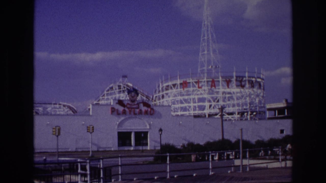 Wider view of the Playland facade, roller coaster, tall tower, railings, and street signals.