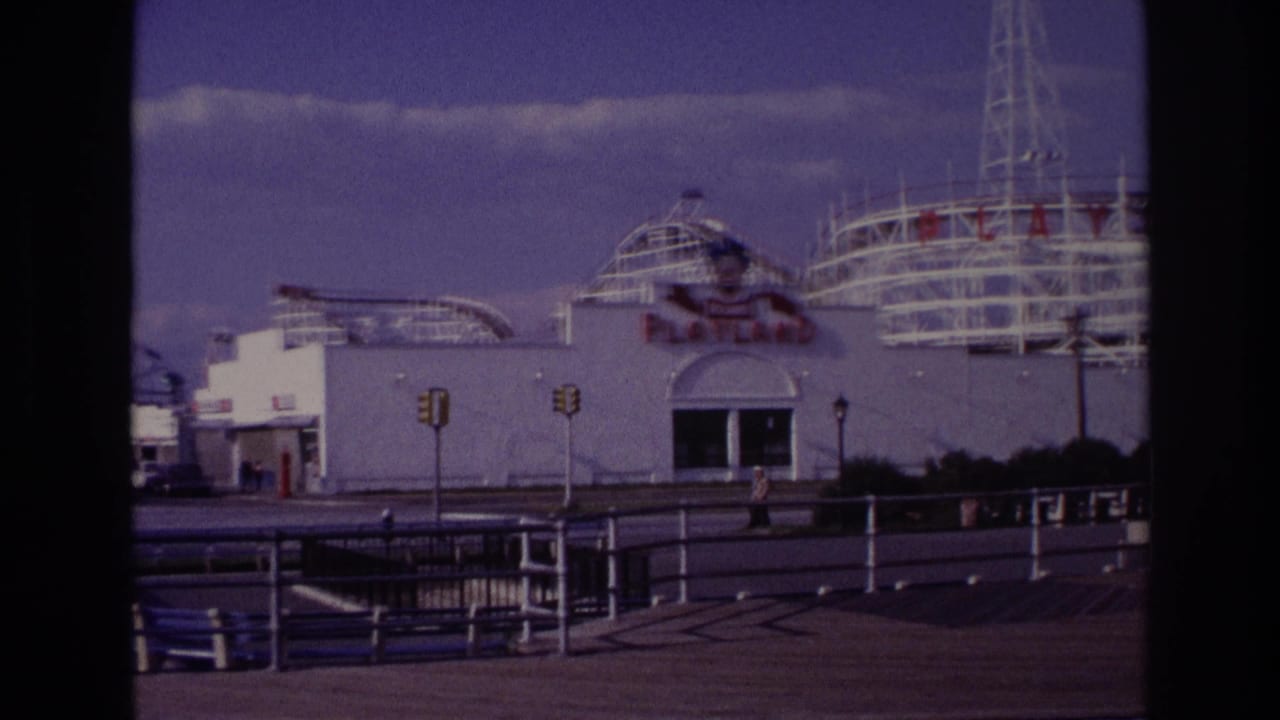 Playland amusement park entrance with rollercoaster tracks, traffic lights, railings, benches, and a pedestrian nearby.