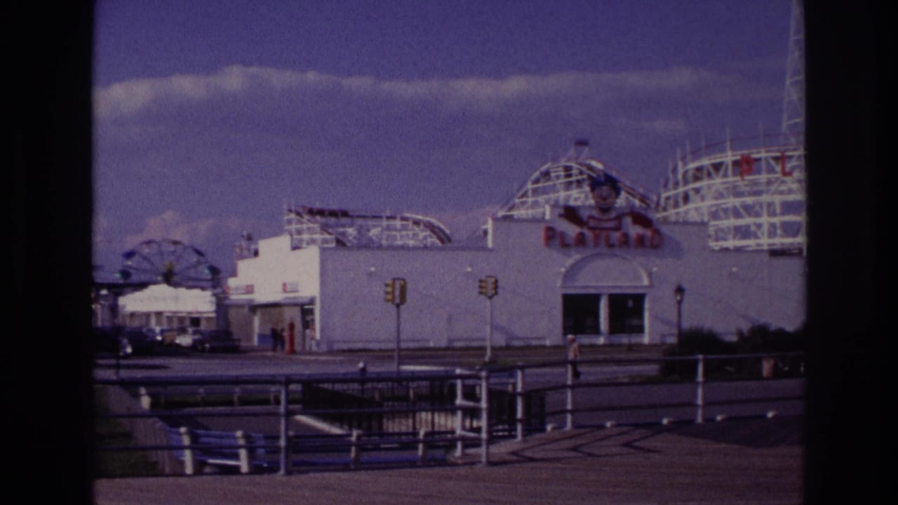 Playland facade, rollercoaster tracks, distant Ferris wheel, traffic lights, railings, benches, and walkway.