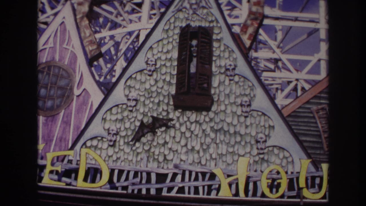 Gothic facade with a central dark window, skull trim, bat silhouette, yellow letters, and metal ride structure behind.