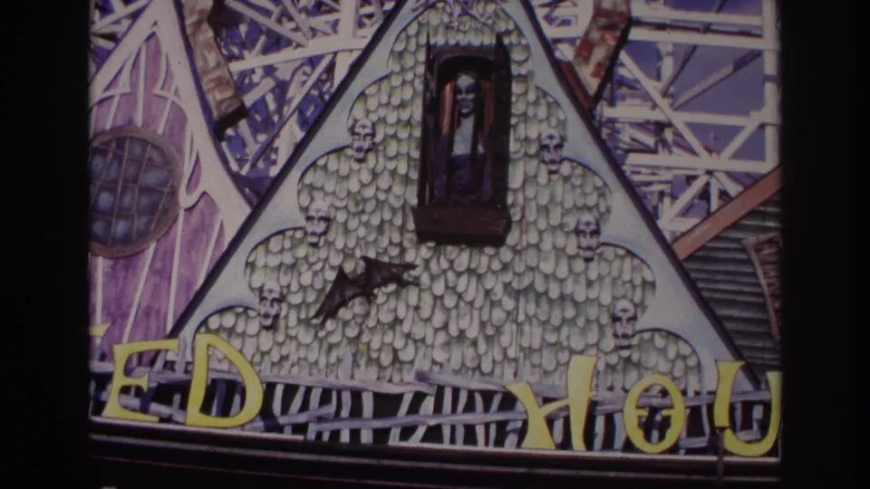 1967 Rockaway Beach 8mm frame showing a spooky attraction facade with a window figure, bat shape, skull trim, and yellow lettering.