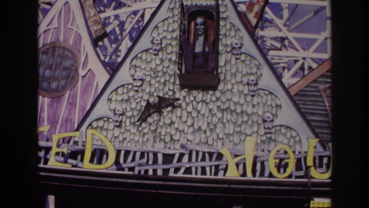 Closer view of the haunted house facade with skulls, bat shape, window figure, and yellow letters.