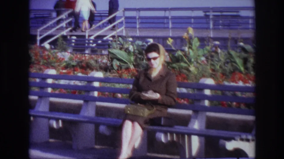 Wider 1967 Rockaway Beach view shows the woman seated on the blue bench while people pass on the raised walkway.