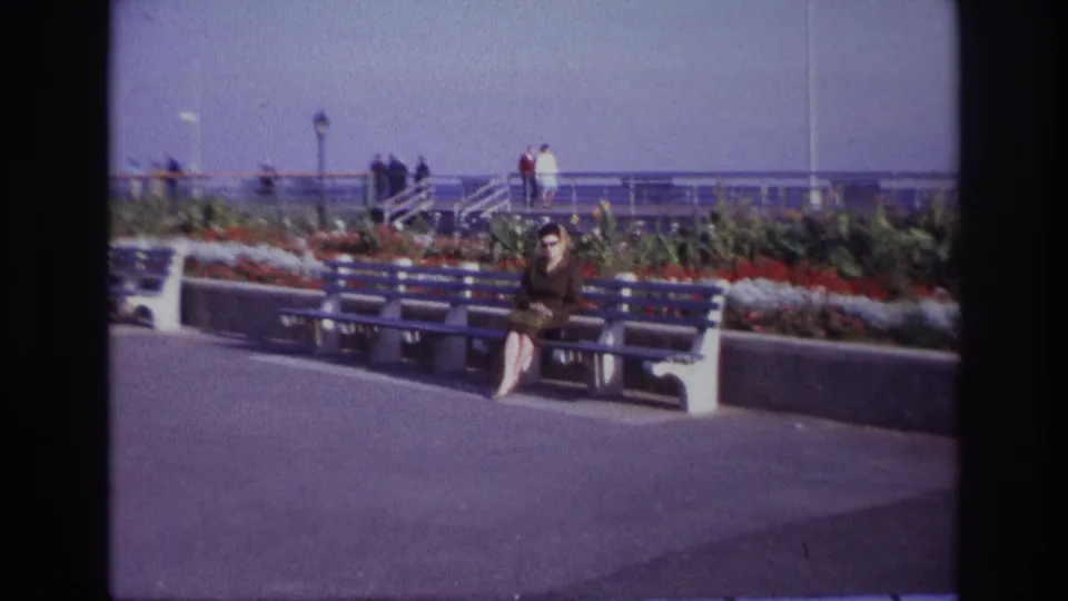 A wider 1967 Rockaway Beach view places the seated woman farther back among benches, bright flower beds, railings and a broad paved promenade.