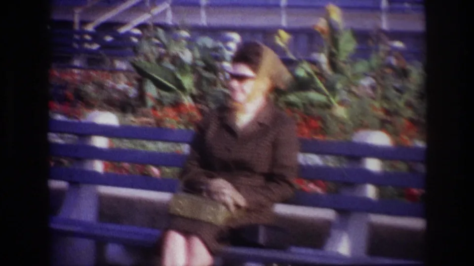 In the 1967 Rockaway Beach clip, the woman sits with her hands near a small clutch while flowers and foliage fill the background.