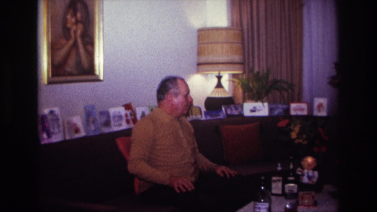 Man turns while sitting on a couch in a living room with bottles and cards nearby.