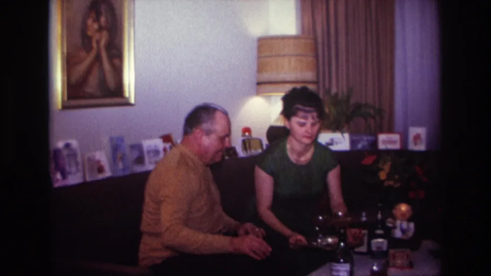 1967 Rockaway Beach home interior with two adults seated beside a low table holding drinks and bottles.